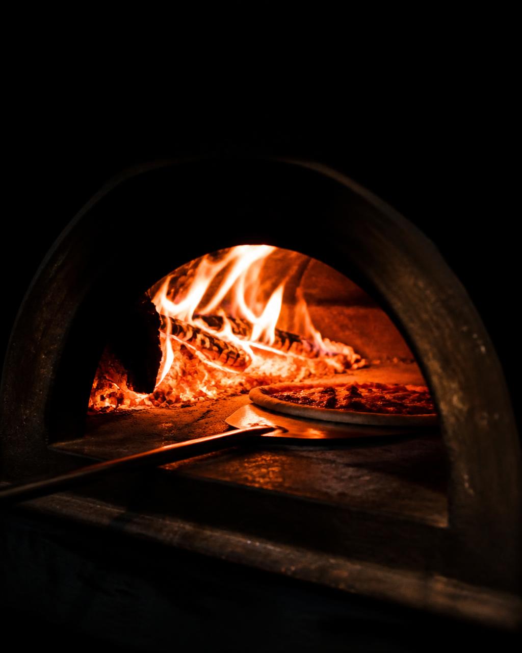 Pizza entrando al horno de leña encendido